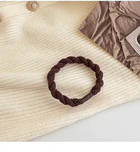 Dettaglio di un elastico per capelli intrecciato marrone caffè su sfondo in maglia bianca