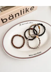 Close-up of five elastic braided hair ties in earthy tones displayed on a ceramic dish