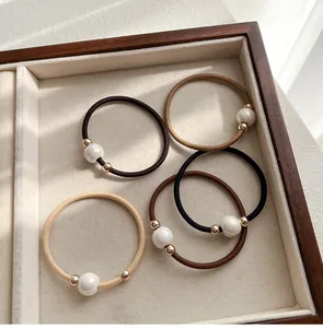 Close-up of five elastic hair bands with pearls in brown tones on a wooden tray