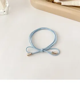 Detail of light blue triple-strand elastic bow hair tie with gold decorative tips