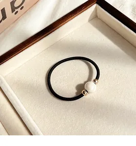 Close-up of elegant black elastic hair tie with white pearl and gold beads in a wooden tray