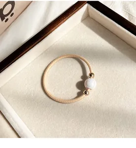 Detail of high-elasticity beige hair tie with white pearl and gold metal beads