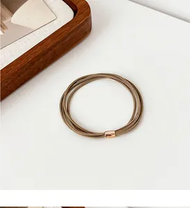 Macro detail of khaki multi-strand elastic hair tie with polished rose gold metal clasp