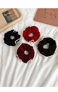 Detailed view of four velvet scrunchies with rhinestones and white piping on fabric