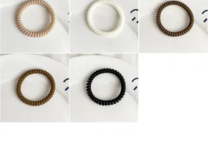 Detail of five matte spiral hair ties in neutral tones on a white ceramic plate