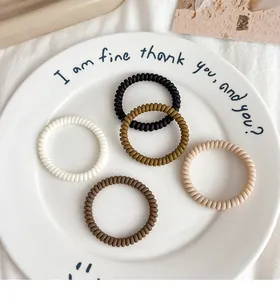 Macro detail of five multi-color spiral hair ties in a minimalist ceramic tray