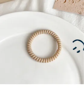 Macro detail of a matte beige spiral hair tie placed on a minimalist ceramic plate