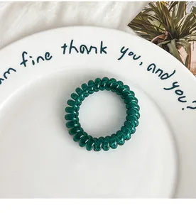 Detail of dark green spiral hair tie on a white ceramic tray with minimalist aesthetic