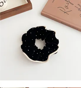Close-up of black velvet scrunchie with white pearl polka dots and contrast stitching