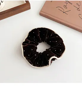 Detail of a brown velvet scrunchie with white beads and wavy beige edges on a white table