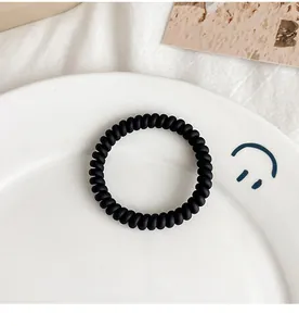 Macro view of matte black spiral hair coil on minimalist ceramic plate and fabric
