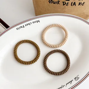 Three earth-toned spiral telephone wire hair ties in a minimalist ceramic dish setting