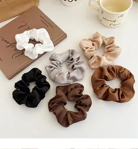 Détail de six chouchous en satin aux tons neutres beige et marron sur un bureau cosy