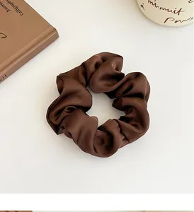 Détail d'un chouchou en satin marron foncé avec texture plissée douce sur fond blanc