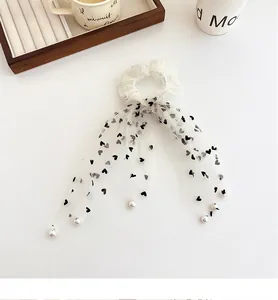 Dettaglio dello scrunchie in rete bianca con cuori neri e ciondoli di perle