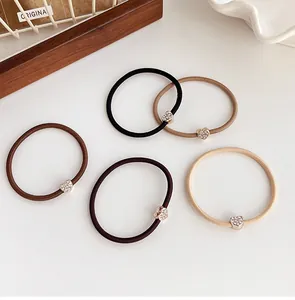Dettaglio di cinque ciondoli a cuore con strass su elastici per capelli color caffè
