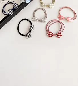 Close-up of colorful gingham bow hair ties in black, red, and pink on a cream surface