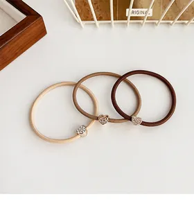 Dettaglio di tre elastici per capelli ad alta elasticità color caffè con ciondoli a cuore
