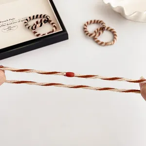 Elastische gedraaide haarring in beige en donker koffie met een rode kraal