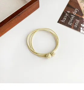 Close-up of beige multi-strand elastic hair ties with woven knots on a white surface