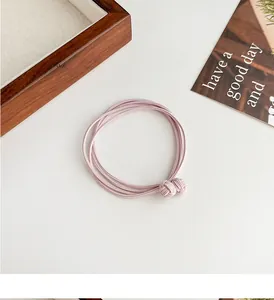 Detail view of light pink multi-strand braided hair tie with a decorative knot on wood tray