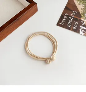 Detail of beige multi-strand elastic hair tie with woven knot balls on white background