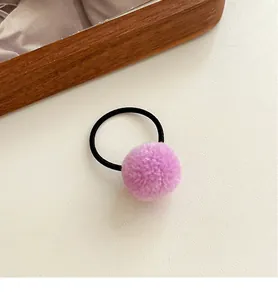 Close-up of pink-purple plush pom-pom hair tie with elastic band on a wooden tray