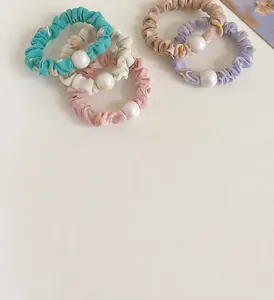 Détail de cinq chouchous floraux avec perles blanches et tissu plissé doux et soyeux