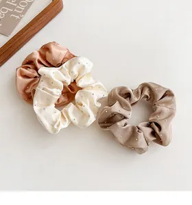 Dettaglio di tre elastici in raso con strass nei colori crema, marrone chiaro e beige