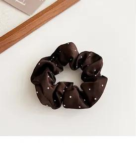 Dettaglio dell'elastico scrunchie in raso marrone con strass lucidi e trama a pieghe