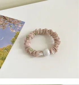 Détail d'un chouchou beige à fleurs avec une grande perle blanche et motif de feuilles