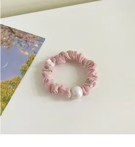 Détail du chouchou floral rose avec une grande perle nacrée sur un bureau blanc