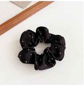 Dettaglio macro dello scrunchie in raso nero con delicate decorazioni a punti d'argento