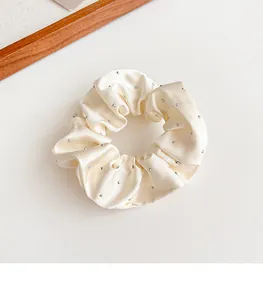 Dettaglio di scrunchie in raso crema con strass che mostra consistenza liscia ed elastica