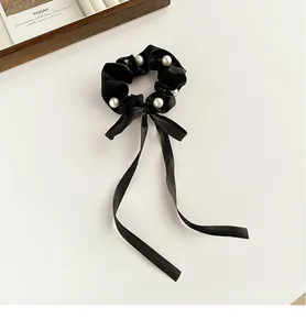 Macro shot of black satin bow hair scrunchie with white pearl accents and long ribbon