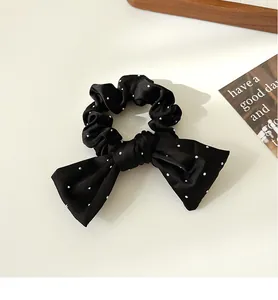 Détail d'un chouchou en satin noir avec nœud et perles blanches sur fond épuré