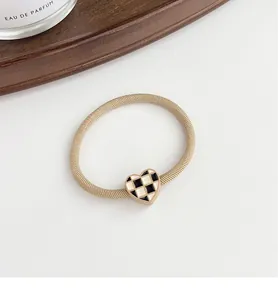 Detail shot of heart-shaped checkerboard pendant on elastic hair tie with gold trim