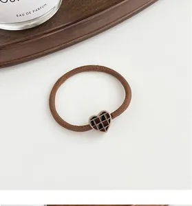 Detail of high elasticity hair tie featuring a retro heart checkered charm in brown
