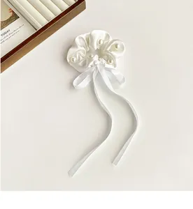 Close-up of white satin scrunchie with elegant ribbon bow and pearl embellishments