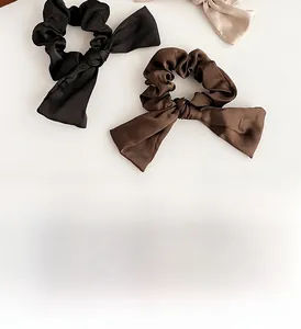 Détail de trois chouchous à nœuds en soie en noir, marron et beige sur fond blanc