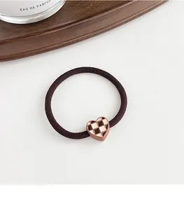 Macro detail of elastic hair tie with brown checkered heart charm on white desk