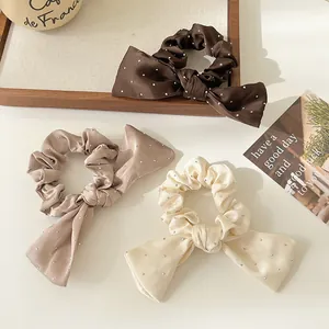 Trois chouchous nœud avec strass en marron, café et crème sur un plateau en bois