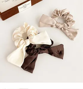 Détail de trois chouchous en satin avec nœuds en doré, blanc et marron café