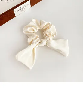 Gros plan du chouchou en satin crème avec longs rubans sur un fond minimaliste