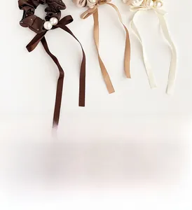 Detailed view of three satin bow hair scrunchies with white pearls in earth tones