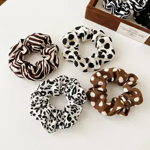 Set of 4 French leopard and zebra pattern scrunchies on a white surface with props