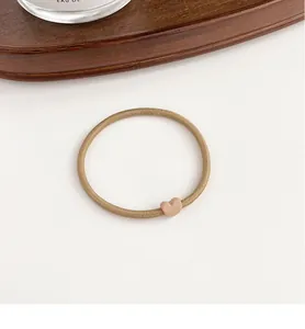 Detail of coffee brown elastic hair tie featuring a matte heart buckle on a wooden tray