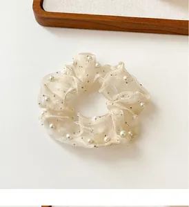Détail d'un chouchou en organza blanc cassé avec perles délicates et sequins