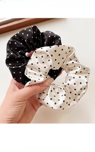 Close-up of black and white polka dot satin scrunchies held by hand in a cozy setting