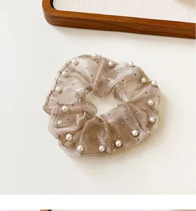 Détail macro du chouchou en organza champagne avec perles blanches et paillettes argentées